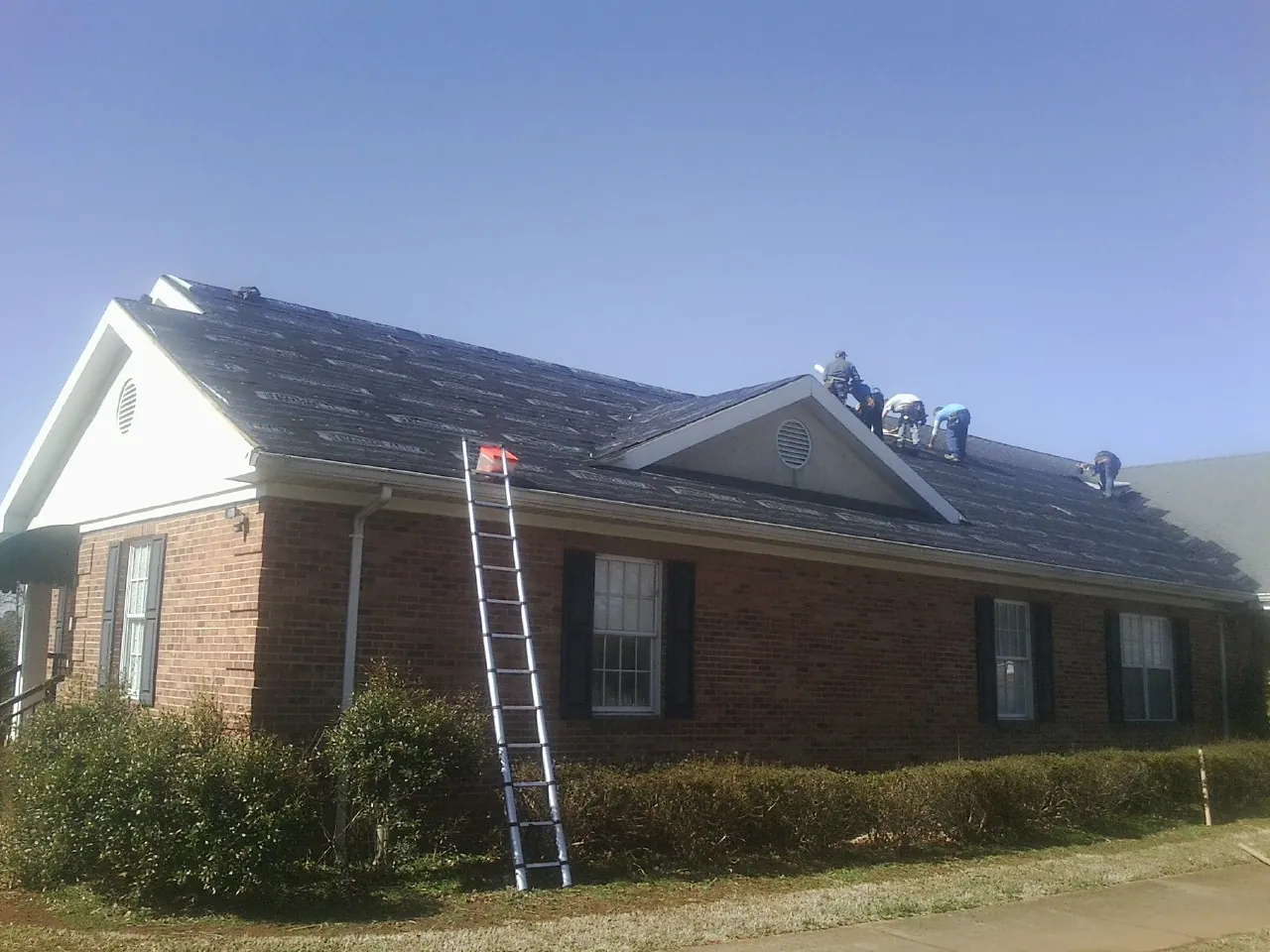 Crew tearing shingles off a brick ranch roof with a ladder set — Metal Roof Repair work by our crew in Coeymans Hollow