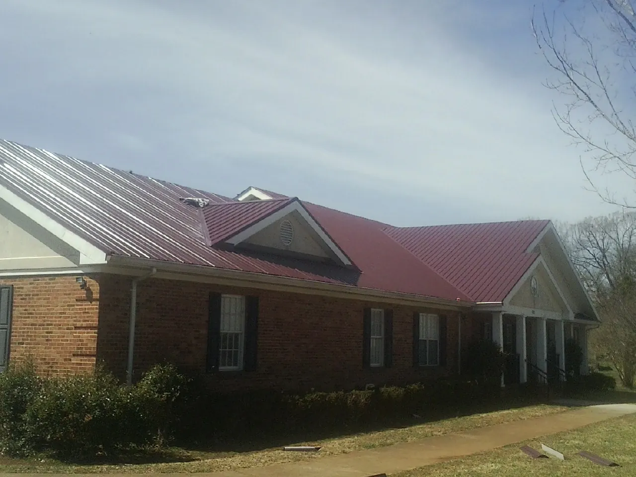 Red metal roof with gabled entries on a long brick building, from a Hail Damage Roof Repair job in Coeymans Hollow