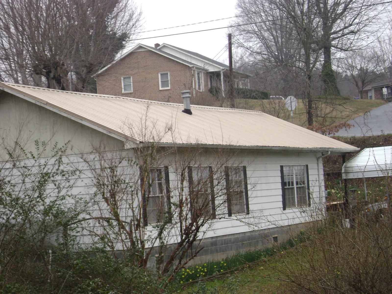 Tan metal roof on a white sided house set into a hillside — Commercial Roofing by Roofing Brothers in Coeymans Hollow